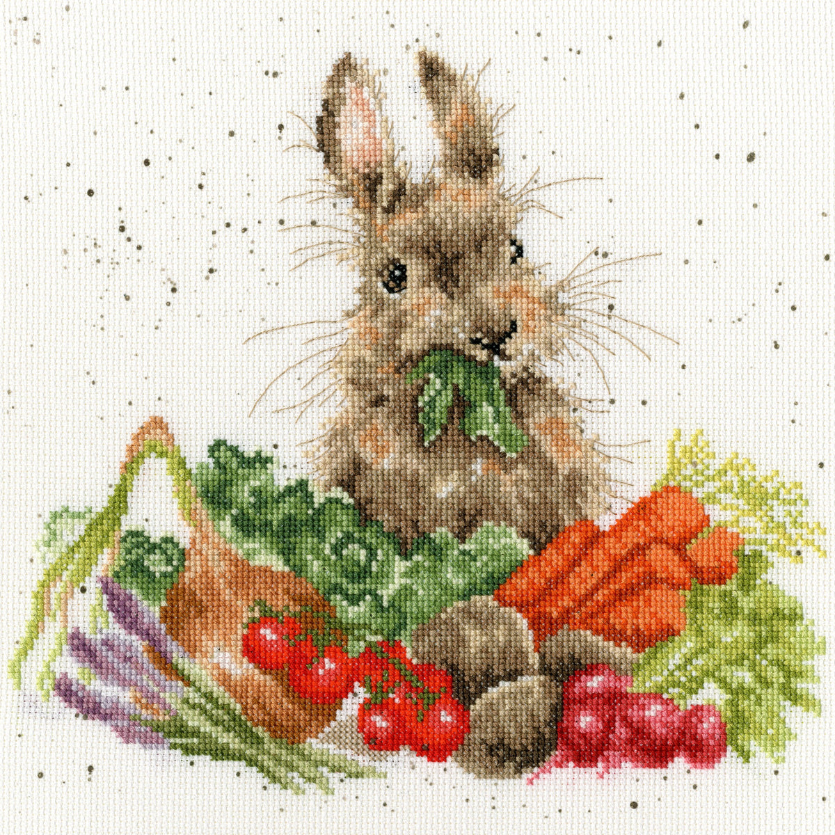 Cross stitch kit featuring a rabbit eating vegetables with colorful garden produce on printed speckled Aida fabric